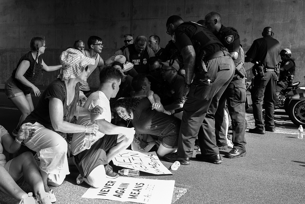 Protesters with Never Again signs being detained by police at an immigration demonstration